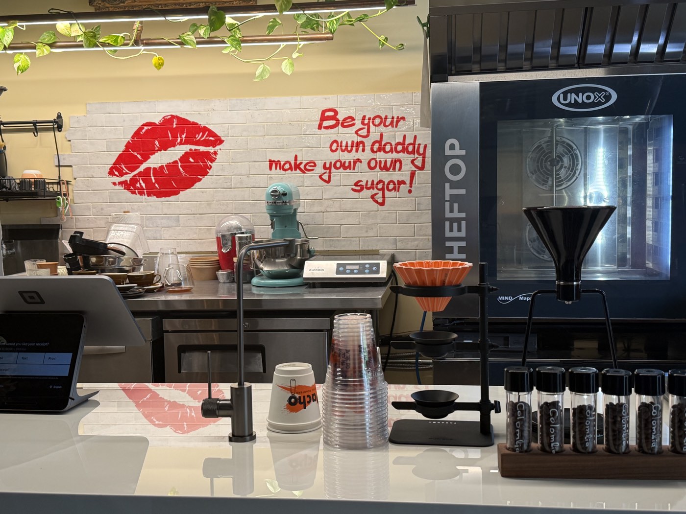 The El Pacho bar with a teal stand mixer, pour-over stand, and a hand-painted wall that reads Be your own daddy, make your own sugar